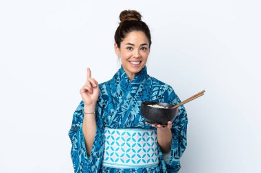 İzole edilmiş beyaz arka planda kimono giyen bir kadın elinde çubuklarla elinde bir kase şehriye tutarken harika bir fikir olduğunu gösteriyor.