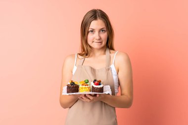 Ukraynalı pasta şefi pembe arka planda izole edilmiş bir kek tutuyor. Şüpheleri var ve kafası karışmış bir yüz ifadesi var.
