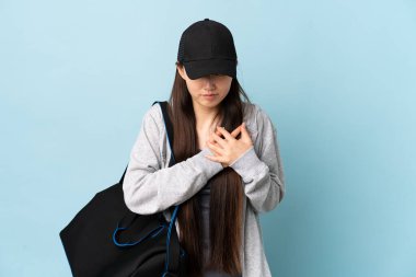 İzole edilmiş mavi arka planda spor çantasıyla genç bir Çinli kadın. Kalbinde ağrı var.