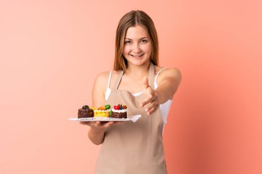 Ukraynalı aşçı, pembe arka planda el sıkışarak izole edilmiş bir kek tutuyor.