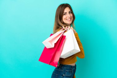 Beyaz kadın mavi arka planda izole edilmiş alışveriş torbaları tutuyor ve gülümsüyor.
