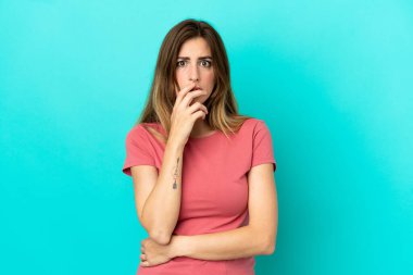 Mavi arka planda izole edilmiş genç beyaz kadın sağa bakarken şaşırdı ve şok oldu.