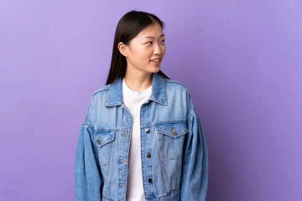 年轻的中国姑娘从孤立的紫色背景上望着侧面 微笑着 — 图库照片