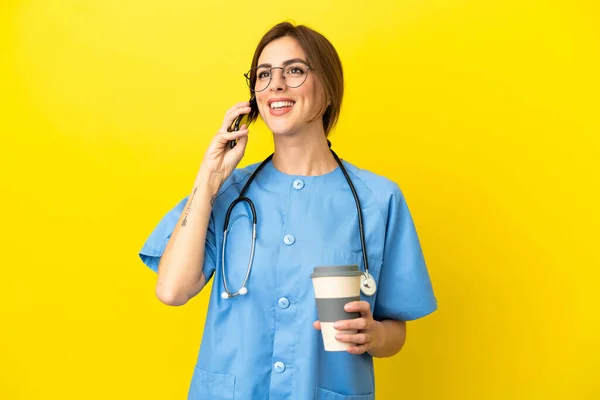 外科医生女医生被隔离在黄色背景下 手里拿着咖啡和手机 — 图库照片