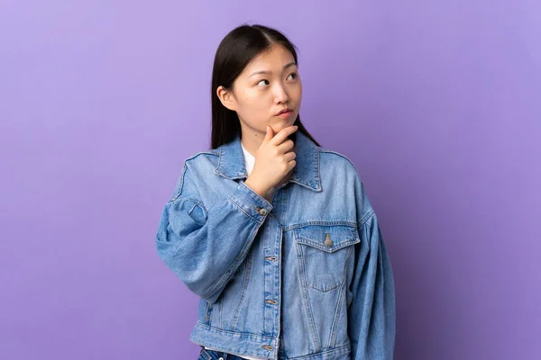 年轻的中国姑娘在紫色的孤立背景上有疑问 — 图库照片