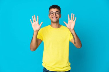 Mavi arka planda izole edilmiş genç Brezilyalı adam parmaklarıyla ona kadar sayıyor.