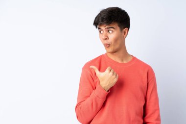 Yakışıklı adam izole edilmiş mavi arka planda mutsuz ve kenarı işaret ediyor.