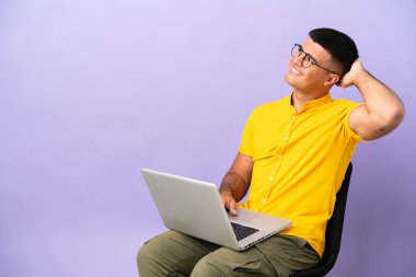 Genç adam dizüstü bilgisayarlı bir sandalyede oturuyor ve bir fikir düşünüyor.