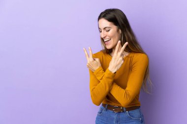 İzole edilmiş arka planda gülümseyen ve zafer işareti gösteren beyaz bir kadın.