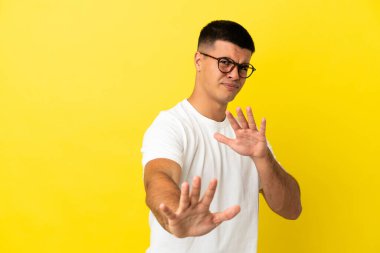 Sarı arka plan üzerinde genç ve yakışıklı bir adam gergin bir şekilde ellerini öne uzatıyor.