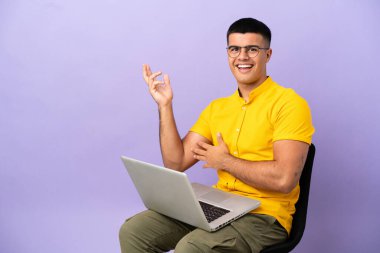 Dizüstü bilgisayarlı bir sandalyede oturan genç adam davet etmek için ellerini yana uzatıyor.