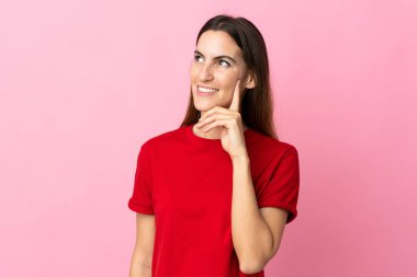 Pembe arka planda izole edilmiş genç beyaz kadın yukarı bakarken bir fikir düşünüyor.
