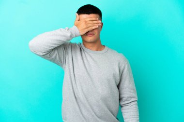 İzole edilmiş mavi arka planda genç yakışıklı adam gözlerini elleriyle kapatıyor. Bir şey görmek istemiyorum.