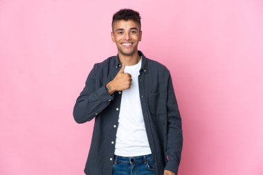 Pembe arka planda izole edilmiş genç Brezilyalı adam baş parmak hareketi yapıyor.