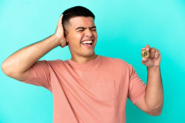 Bitcoin tutan genç yakışıklı adam izole edilmiş mavi arka planda çok gülümsüyor.