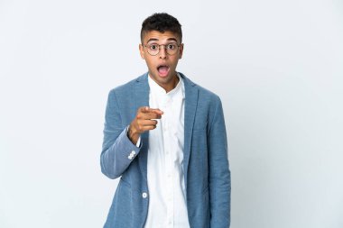 Genç Brezilyalı iş adamı beyaz arka planda izole edilmiş şaşırmış ve ön tarafı işaret ediyor.