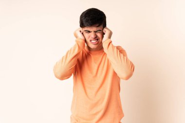 İzole edilmiş bej arka planı olan yakışıklı adam hayal kırıklığına uğramış ve kulaklarını kapatmış.