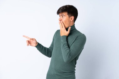 Yalıtılmış mavi arkaplan üzerinde yakışıklı bir adam işaret ederken sürpriz yüz ifadesi ile