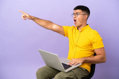 Genç adam bir sandalyede oturuyor ve dizüstü bilgisayarını gösteriyor.