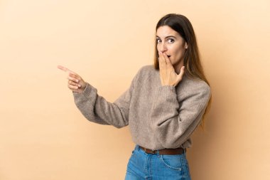 İzole edilmiş arka planda genç beyaz kadın sürpriz bir ifadeyle işaret ederken...
