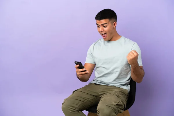 Jovem Sentado Uma Cadeira Sobre Fundo Isolado Surpreendido Enviando Uma — Fotografia de Stock