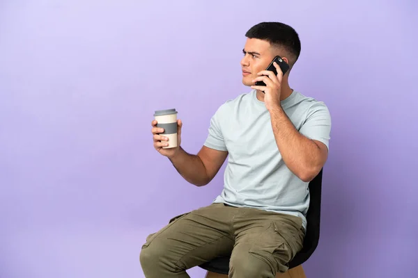 Joven Sentado Una Silla Sobre Fondo Aislado Sosteniendo Café Para —  Fotos de Stock