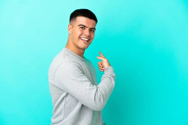 Joven Hombre Guapo Sobre Fondo Azul Aislado Apuntando Hacia Atrás —  Fotos de Stock