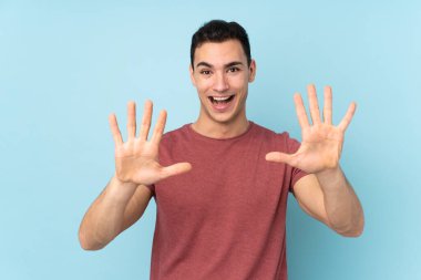 Mavi arka planda izole edilmiş beyaz tenli yakışıklı adam parmaklarıyla 10 'a kadar sayıyor.