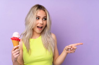 İzole edilmiş mor arka planı olan genç kız şaşırdı ve parmağını yana çevirdi.