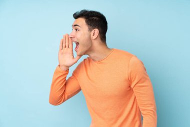 Beyaz tenli yakışıklı adam mavi arka planda izole edilmiş ve ağzı sonuna kadar açık bağırıyor.