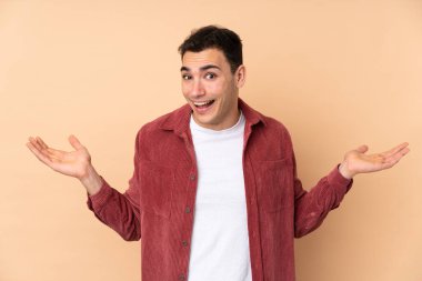 Beyaz tenli yakışıklı adam, bej arka planda izole edilmiş, şok olmuş bir yüz ifadesi var.