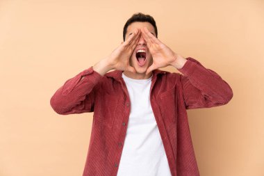 Beyaz tenli yakışıklı adam bej arka planda izole edilmiş bağırıyor ve bir şeyler söylüyor.