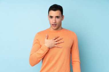 Mavi arka planda izole edilmiş beyaz, yakışıklı genç adam sağa bakarken şaşırmış ve şok olmuştu.