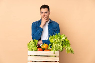 Bej arka planda izole edilmiş bir kutuda taze sebze toplayan çiftçi sağa bakarken şaşırmış ve şok olmuştu.