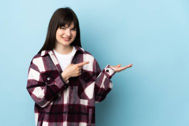 Mavi arka planda izole edilmiş genç Ukraynalı kız bir ilan vermek için avucunun içinde hayali bir kopyalama alanı tutuyor.