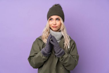 Kışlık şapkalı genç sarışın kız, izole edilmiş mor arka planda bir şeyler çeviriyor.