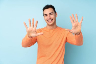 Mavi arka planda izole edilmiş beyaz tenli yakışıklı adam parmaklarıyla 10 'a kadar sayıyor.