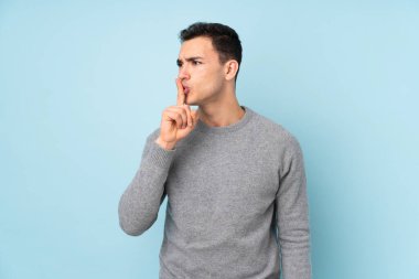 Mavi arka planda izole edilmiş beyaz, yakışıklı genç bir adam sessizlik hareketi yapıyor.