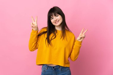 Pembe arka planda izole edilmiş genç Ukraynalı kadın iki eliyle zafer işareti gösteriyor.