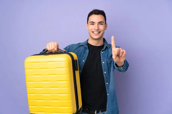 年轻的白种人英俊男子 穿着紫色背景的衣服 带着旅行箱外出度假 数着一个 — 图库照片