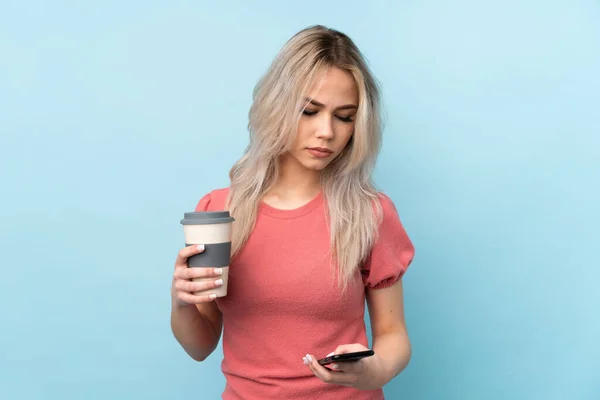 Ragazza Adolescente Sfondo Blu Isolato Tenendo Caffè Portare Cellulare — Foto Stock