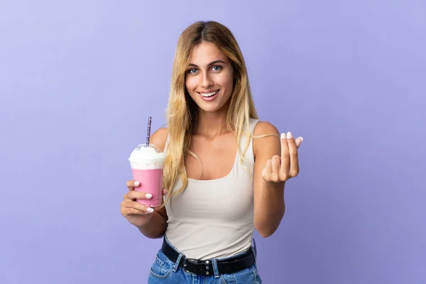 年轻的金发乌拉圭女子与草莓奶昔隔离紫色背景赚钱的姿态 — 图库照片