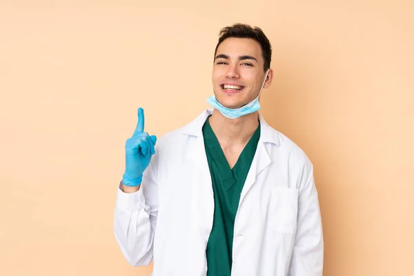Jovem Dentista Homem Segurando Ferramentas Isoladas Fundo Bege Mostrando Levantando — Fotografia de Stock