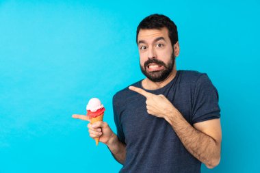 Kornet dondurması olan genç adam mavi arka planda korkmuş ve kenarı işaret ediyor.