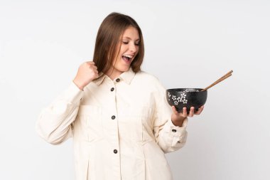 Beyaz arka planda izole edilmiş genç beyaz kız elinde çubuklarla elinde bir kase erişte tutarak zaferi kutluyor.