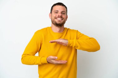 Beyaz arka planda izole edilmiş genç Brezilyalı bir adam bir ilan vermek için avucunun içinde hayali bir mekan tutuyor.