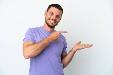 Beyaz arka planda izole edilmiş genç Brezilyalı bir adam bir ilan vermek için avucunun içinde hayali bir mekan tutuyor.