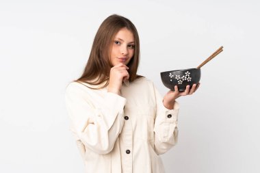 Beyaz arka planda izole edilmiş genç beyaz bir kız elinde çubukla bir kase erişte tutarken bir fikir üretiyor ve etrafına bakıyor.