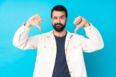 Mavi arka planda beyaz kadife ceketli genç ve yakışıklı bir adam baş parmağını aşağı gösteriyor.