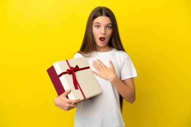 Sarı arka planda bir hediye tutan küçük kız şaşırdı ve şaşırdı.